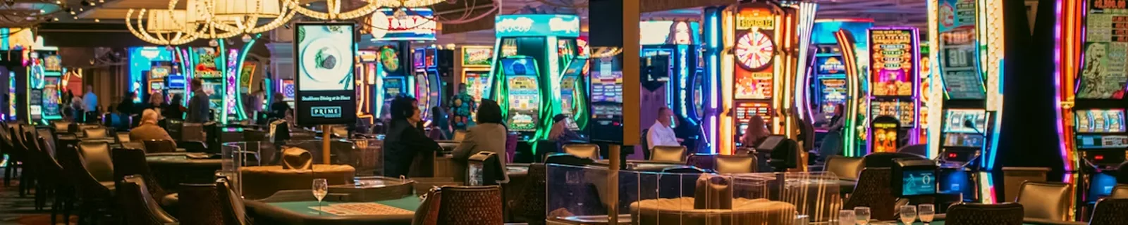 A casino floor with slot machines and table games under chandeliers