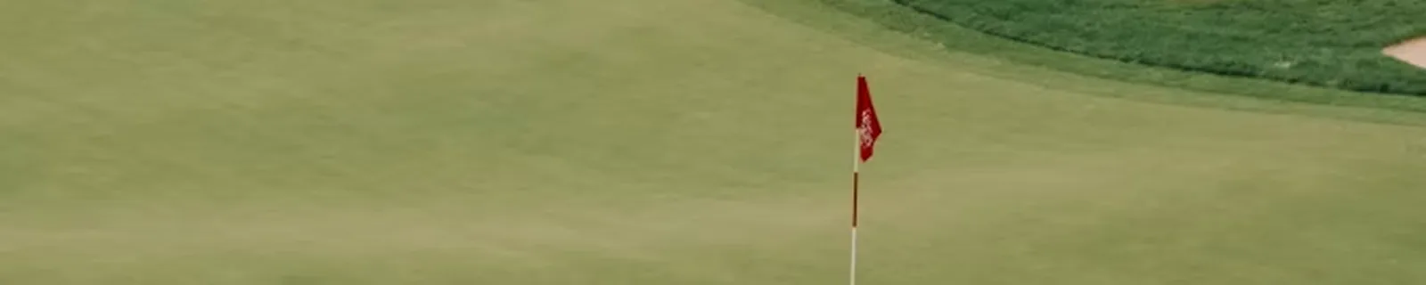 A golfer on a green beside a bunker with the flag in view