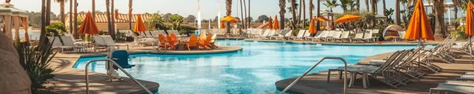 A resort pool lined with palm trees, umbrellas and loungers